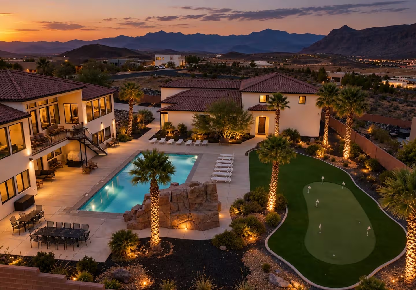 Our resort-style group house at sunset, with an illuminated pool, putting green, palm trees, and mountain views